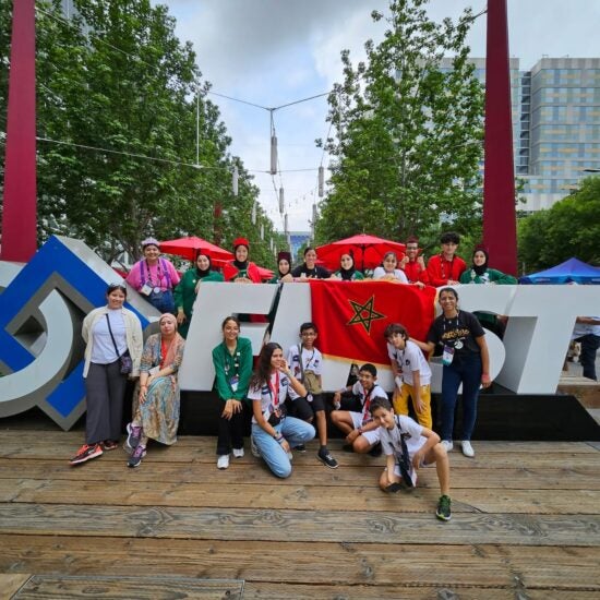 A group of young people posing in front of a FIRST Robotics sign.