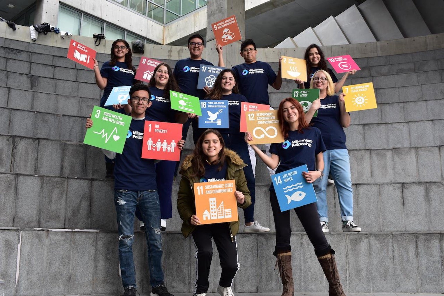 A group of young people standing posed for a photo outside. Each holds a small poster with one of the UN Sustainable Development Goals on it.